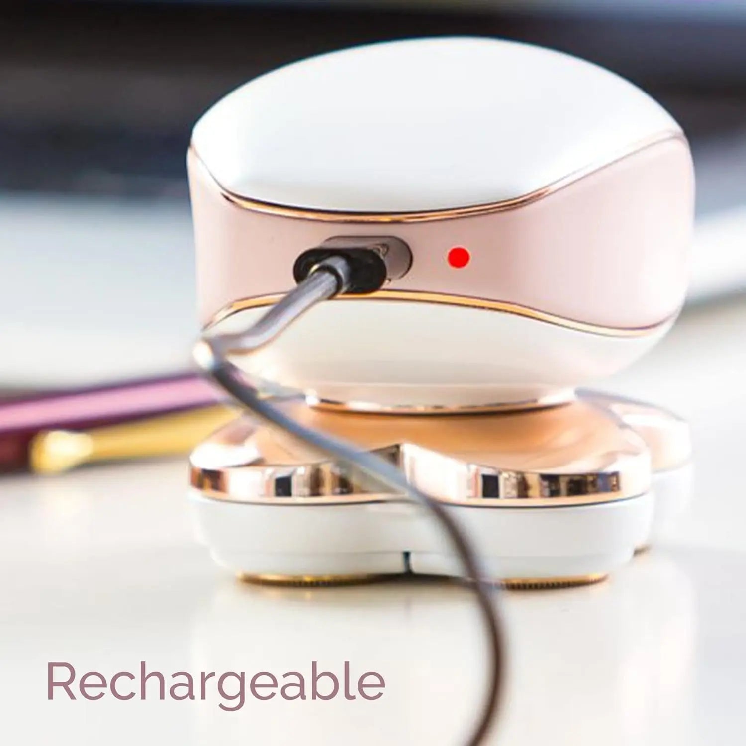 White and gold electronic device with a charging cable, on a blurred background.