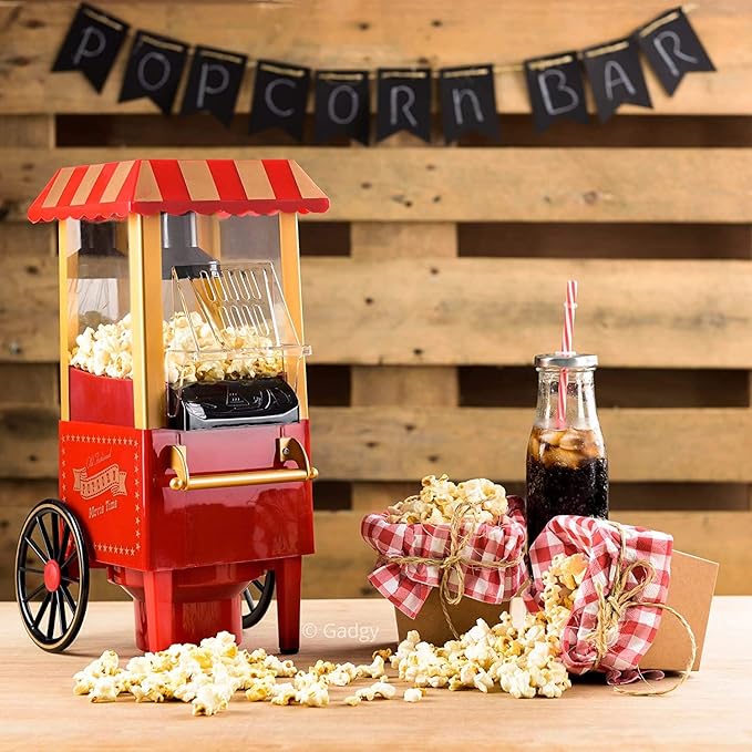Red popcorn machine with popcorn and a bottle of soda on a wooden table, against a wooden wall with 'Popcorn Bar' banner.