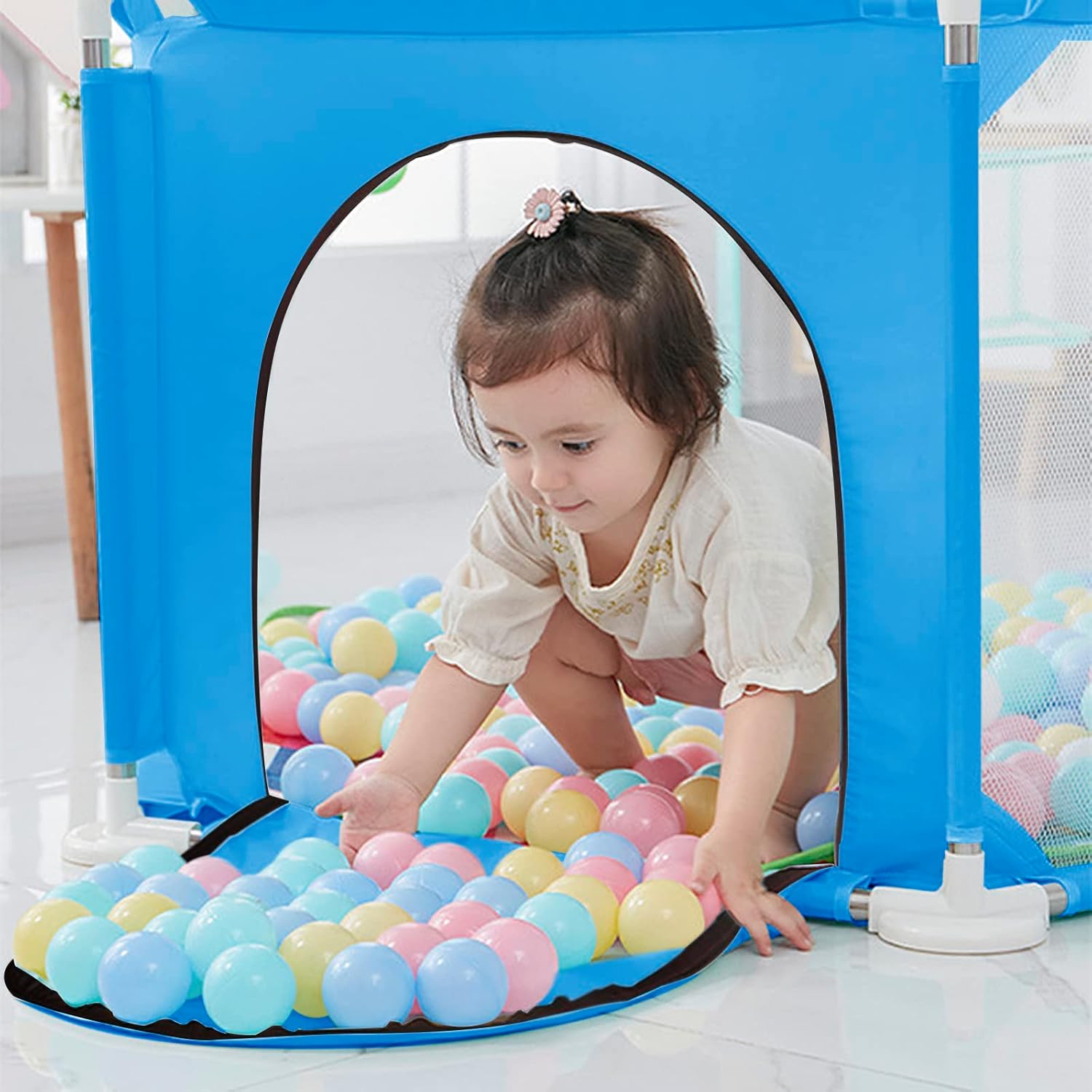 Child playing with colorful balls inside a blue playpen.