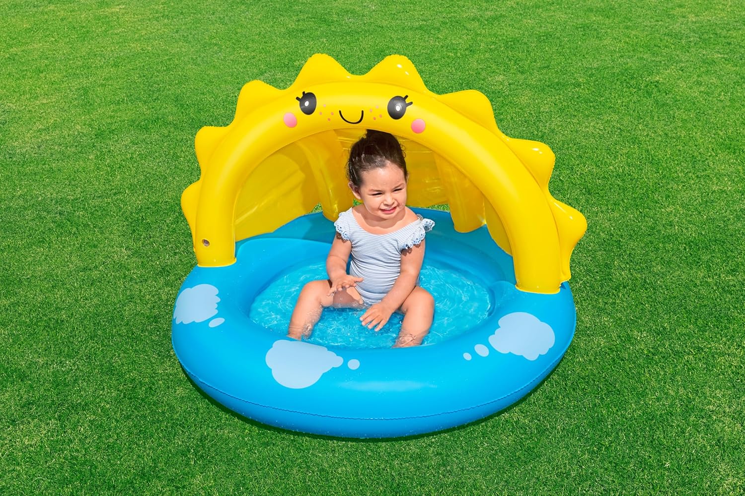 Child sitting in a yellow inflatable sun-shaped pool on a grassy background