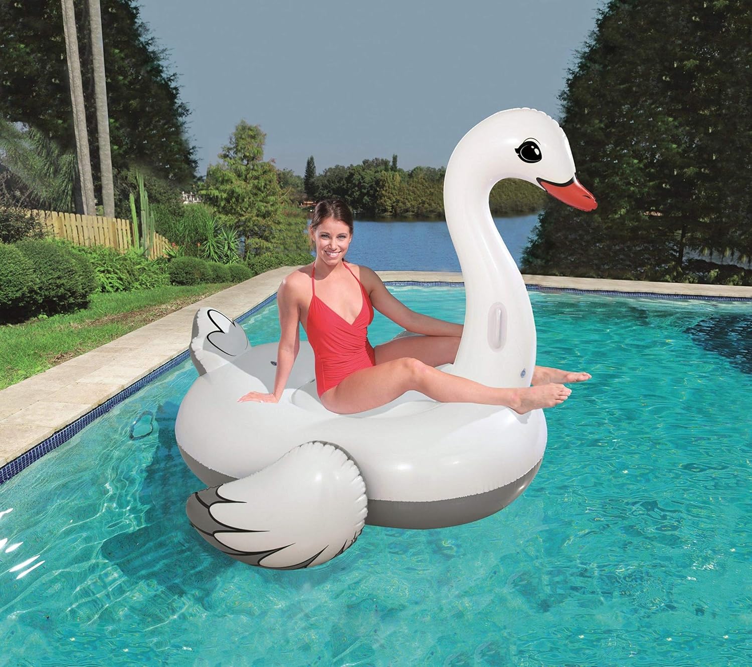 Woman in a red swimsuit sitting on a large inflatable swan pool float in a pool.