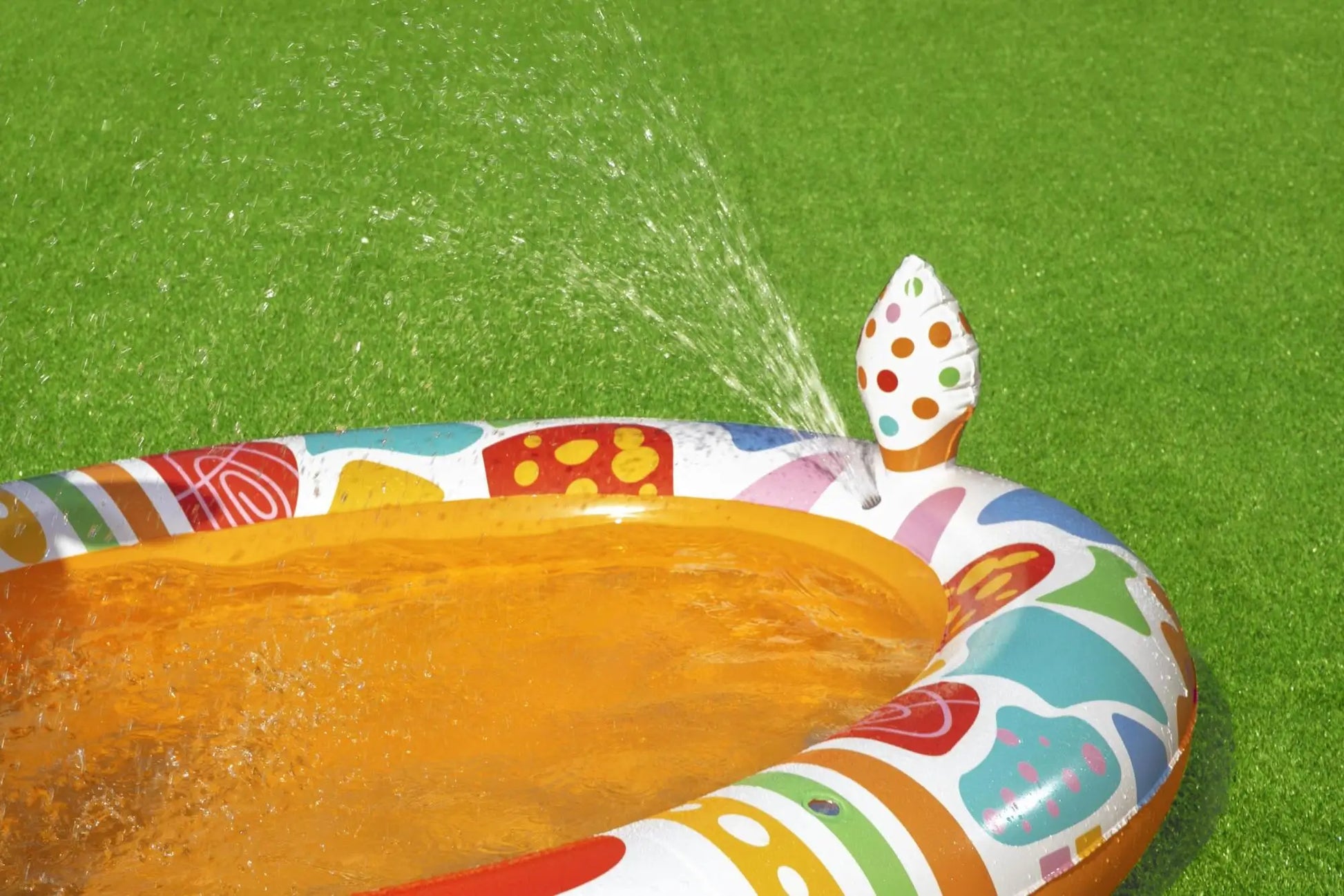 Colorful inflatable pool with a sprinkler on a grassy background